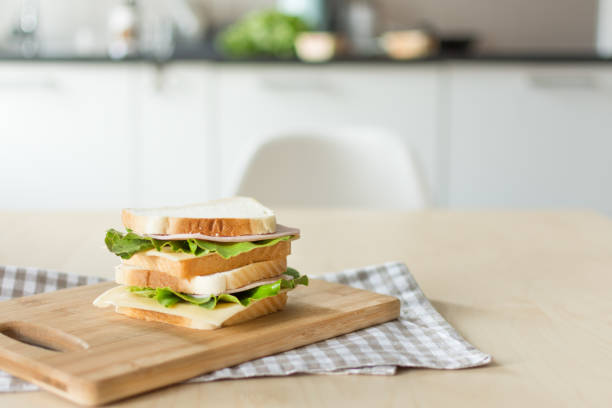 Sandwich with cheese and ham on cutting board on the table in the bright kitchen.