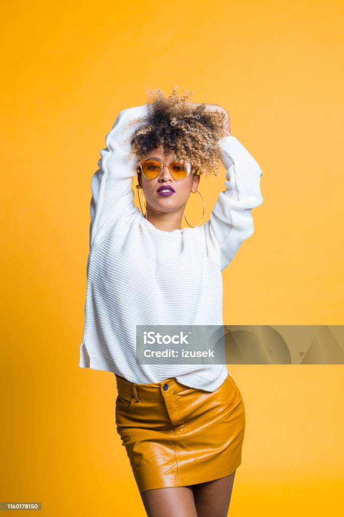 Stylish young african female model Portrait of stylish young african female model posing on yellow background Yellow Stock Photo
