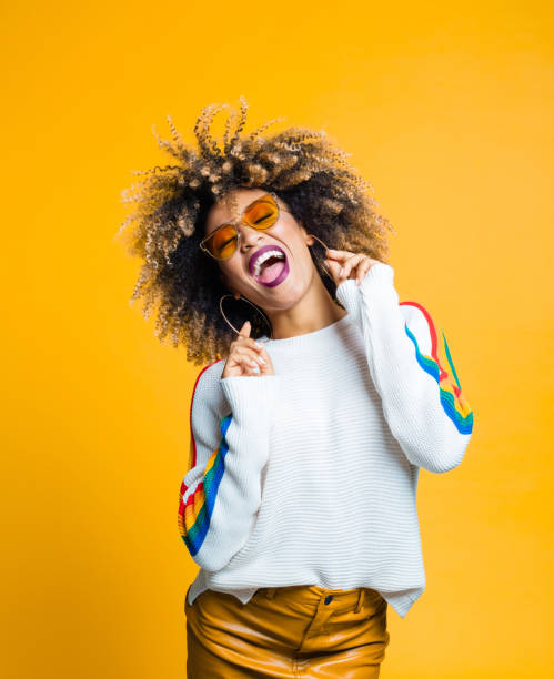 Stylish woman enjoying in studio Portrait of stylish afro young woman enjoying against yellow background cool attitude stock pictures, royalty-free photos & images