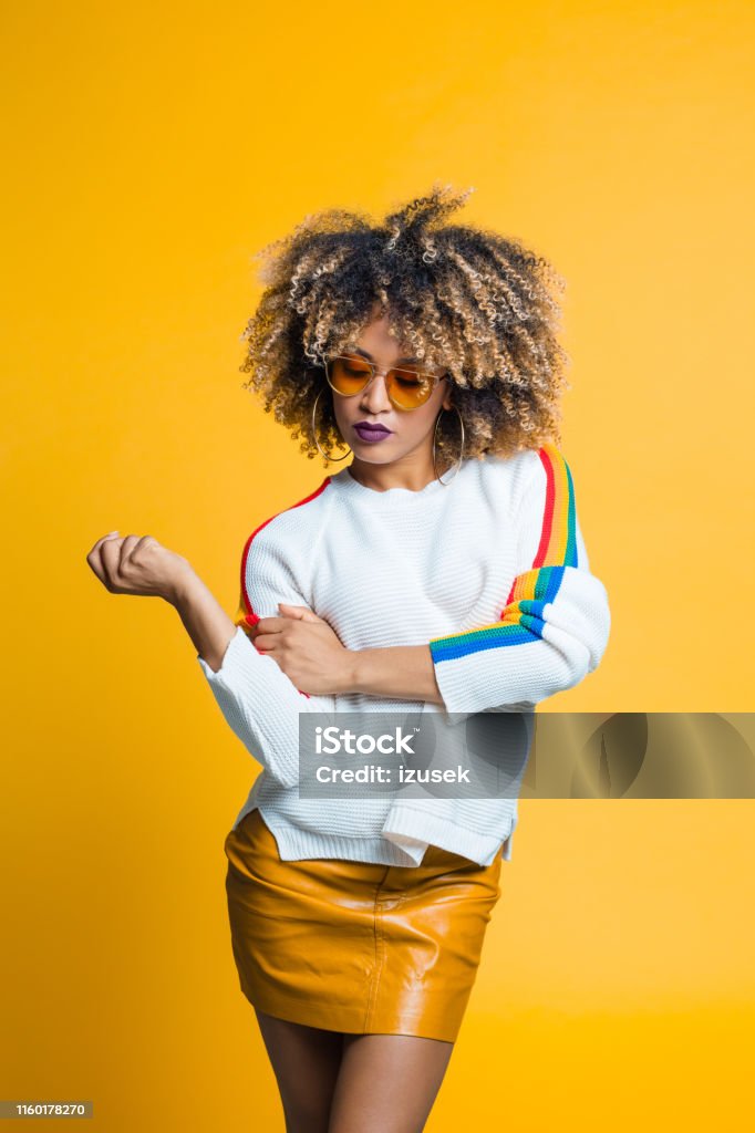 Stylish and trendy young woman Portrait of trendy young african woman standing against yellow background 1960-1969 Stock Photo
