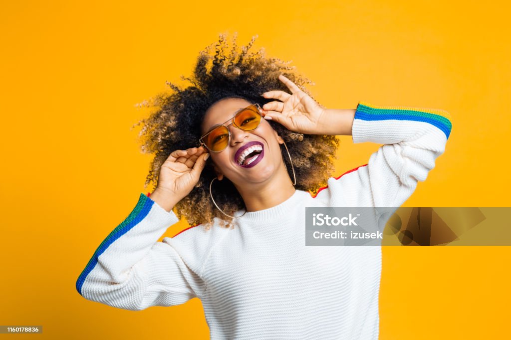 Sixties stylish woman Portrait of stylish afro young woman with sunglasses laughing against yellow background Women Stock Photo