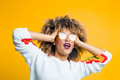 Portrait of funky young afro girl standing against yellow background with hand in hair and looking away