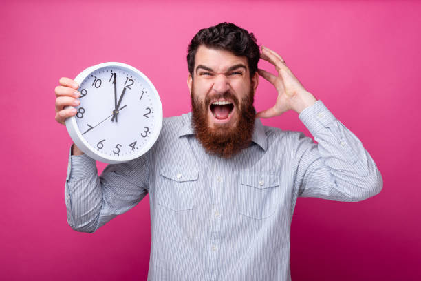 istock Time runs! I'm late. Young bearded man is stressed, holding a white clock and an hand on his head, screaming mad. 1160180551