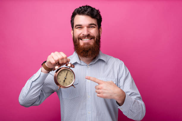 Smiling man with beard in casual pointing at alarm watch stock photo