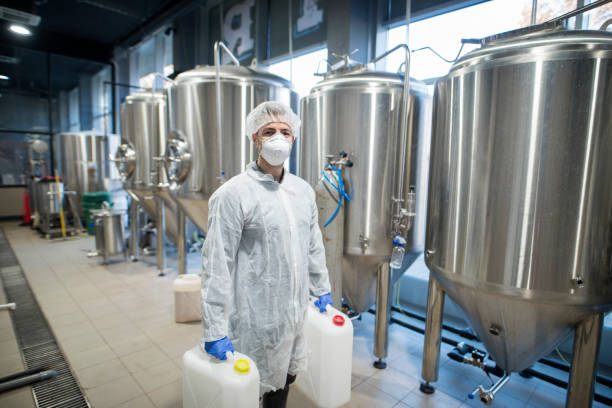 istock Industrial worker technologist in white protective suit with hairnet and mask holding plastic cans with chemicals in food factory production line. 1160180807