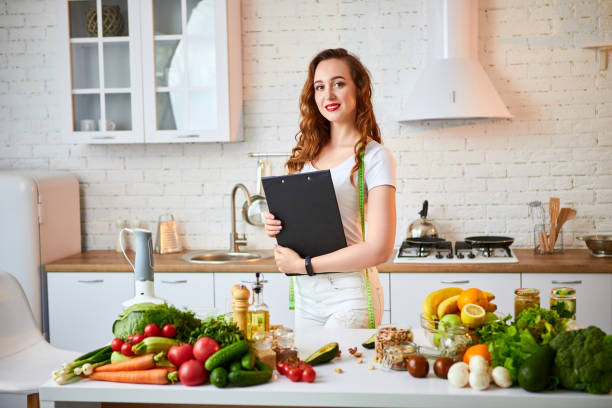 istock Young beautiful woman using tablet while cooking in the modern kitchen. Healthy eating, vitamins, dieting, technology and people concept. Losing Weight 1160181381