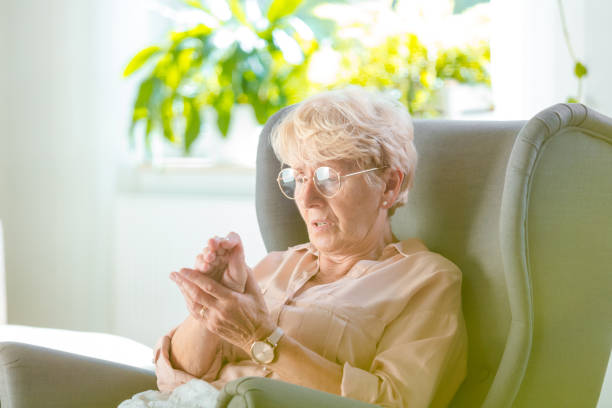 Elderly woman feeling numbness in her hand Elderly woman suffering from pain in hand at home, she is sitting in armchair in her room parkinsons disease photos stock pictures, royalty-free photos & images