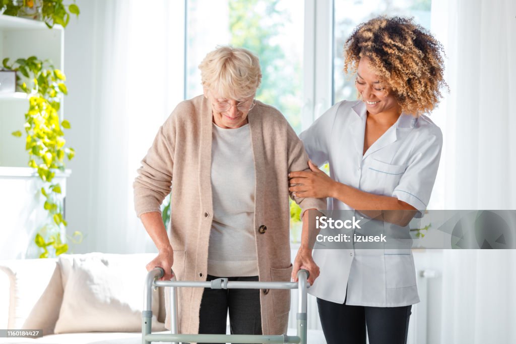 Cheerful friendly nurse helping elderly woman Cheerful friendly nurse helping senior woman to use walking frame Senior Adult Stock Photo