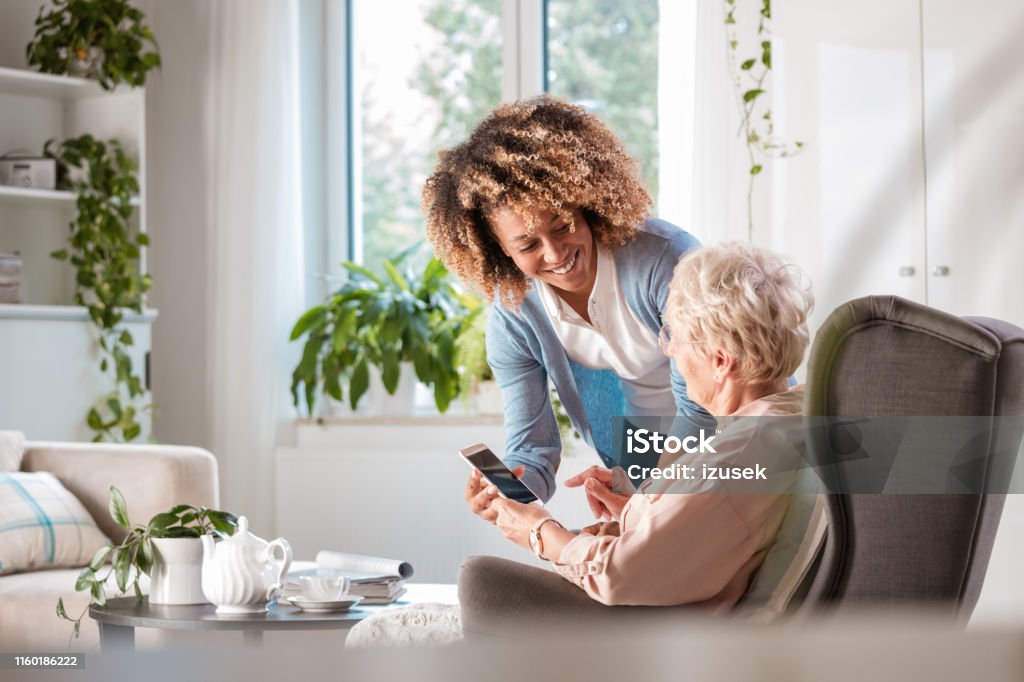 Home caregiver assisting senior woman Female home caregiver helping senior woman in using smart phone Senior Adult Stock Photo