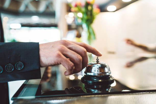 A man ringing the reception bell A close up photo of a man's hand, wearing a suit with buttons on a sleeve, pressing the button with his index finger, ringing a bell on a reception of a modern hotel. bellhop stock pictures, royalty-free photos & images