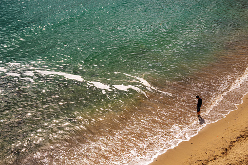 Sestri Levante, Genoa / Italy - April 26 2019: View from above of a sandy beach with the silhouette of a young man standing on the water's edge