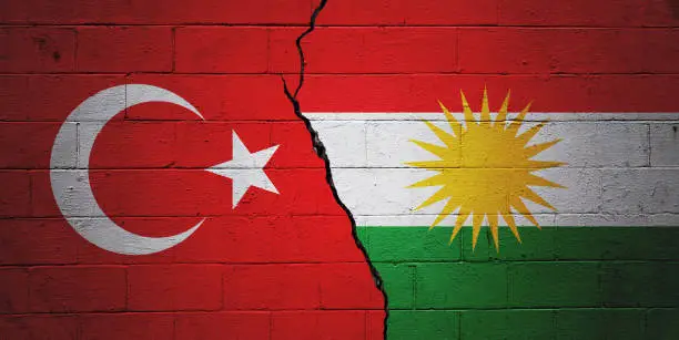 Cracked brick wall painted with a Turkish flag on the left and a Kurdish flag on the right.