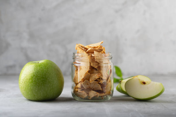 Apple chips in a jar and pieces of this fruits on a table