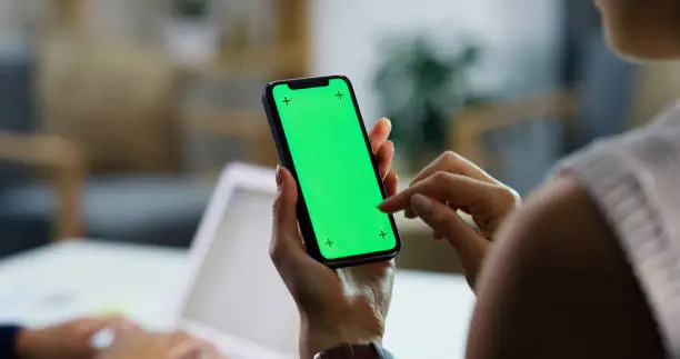 Closeup shot of an unrecognisable businesswoman using a cellphone with a green screen in an office