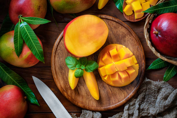 fruits tropicaux : mangues coupées en tranches dans une plaque en bois sur une table dans la cuisine rustique - mangue photos et images de collection