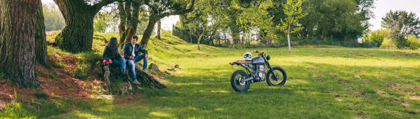Young couple resting from a motorcycle trip having a beer outdoors