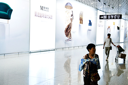 Newly arrived passengers walking through the colourful arrival hall of Shenzhen Bao'an International Airport (IATA: SZX, ICAO: ZGSZ), China. Skygarden ad banner at the background