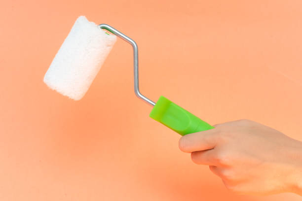 istock Female hand holding paint roller isolated over orange background 1160207963