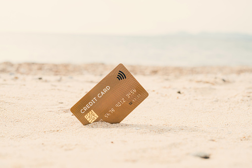 Gold contactless credit card stuck in the sand on seaside