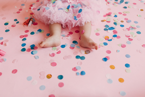 Photo of a little baby girl, celebrating her first birthday cowered in confetti. Studio shot.