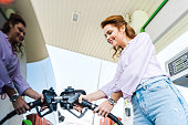 low angle view of happy woman holding fuel pump while refueling car with benzine