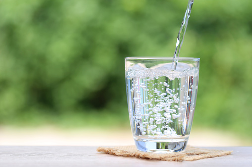 Glass of freshly poured water on the table with nature in the background