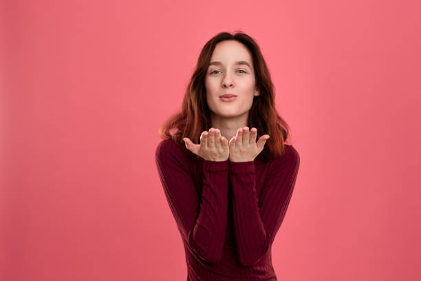 istock Happy young lady standing isolated over dark pink background while sending romantic hand kisses. 1160216975