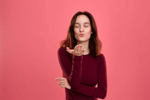istock Happy young lady standing isolated over dark pink background while sending romantic hand kisses. 1160216988