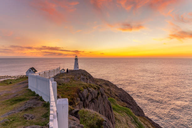 Soft pink and orange clouds light up the sky before sunrise over a white lighthouse sitting at the edge of a rocky cliff. Cape Spear National Historic Site, St Johns Newfoundland. newfoundland and labrador photos stock pictures, royalty-free photos & images
