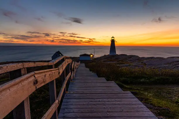 Photo of Beautiful sunrise over a white lighthouse sitting at the edge of a rocky cliff.