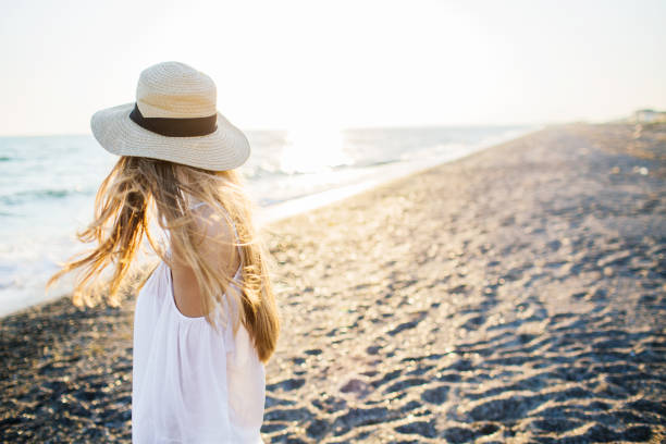 Young attractive long haired blonde girl in straw hat relaxing at the beach at sunset. Soft sunset light.
