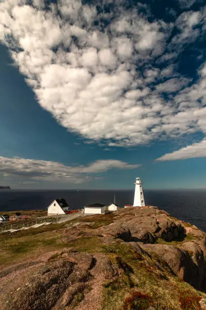 Photo of Dramatic sky over a white lighthouse at the edge of a cliff.
