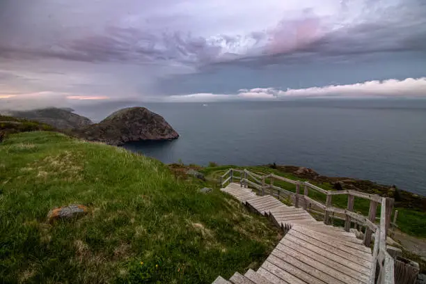 Photo of A wooden staircase leading down to a dramatic coastal seascape with ominous clouds and fog rolling in.