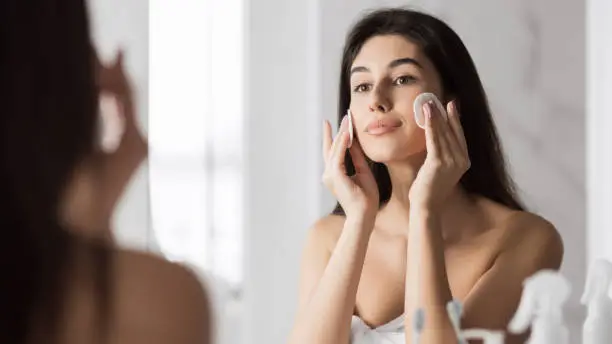 Young cute woman remove makeup , cleaning face with cotton pads looking in mirror at bathroom. Pure healthy skin concept