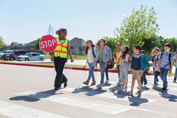 o protetor de cruzamento fêmea que ajuda escolares cruza a rua - crossing guard - fotografias e filmes do acervo