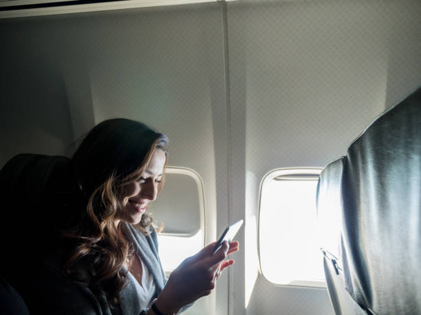 istock Sitting by airplane window, young woman smiles at text message 1160223614