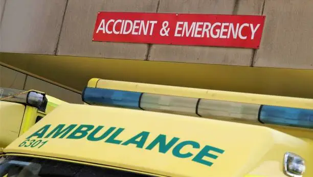 An ambulance waiting outside an NHS hospital in Poole, Dorset, UK underneath an accident and emergency sign on the overhang