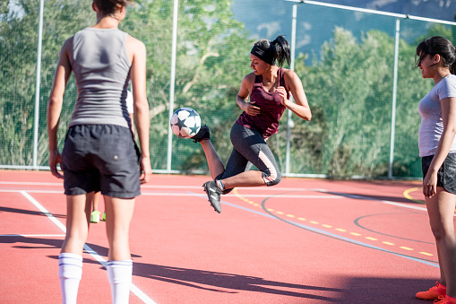Female soccer player performing a trick with ball. Fit women are playing soccer together at court. They are in sportswear.