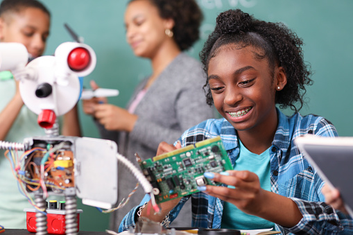 Junior high school age, African American teenage girl works on building a robot in technology class in school classroom setting.  STEM topics.