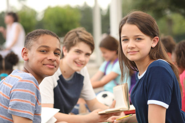 Group of junior high school children, teenage friends studying on campus. Mixed age, multi-ethnic group of junior high school age student friends talk, study together outside the school building. Caucasian, latin, and african descent teenagers. boy and girl reading stock pictures, royalty-free photos & images