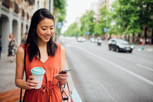 Young woman walking on the street Happy young woman walking on the city street after shopping and using her smartphone asian woman stock pictures, royalty-free photos & images