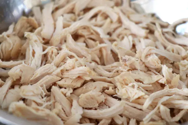 Cooked chicken that is shredded in a container. Shredded chicken in the cup.