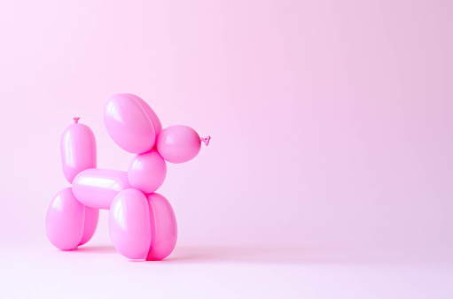Pink balloon in the shape of a dog on a mint-pink background.
