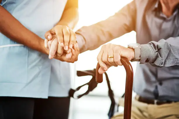 Cropped shot of a nurse holding hands with a senior man using a cane