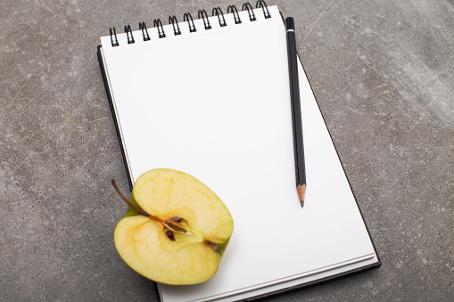 Diet diary Healthy lifestyle concept, white notepad with apple on grey table, top view