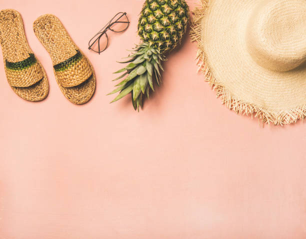 Summer apparel items. Flat-lay of summer flip flops, sunglasses, straw sunhat and fresh pineapple over pastel pink background, top view, copy space. Summer beach vacation concept