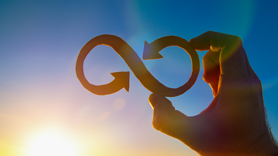 A symbol of infinity in the hand of a man against the sky and the glare of the sun, business concept idea.