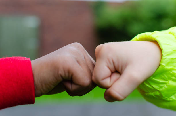 Two children of different races greeting each other with fist bump. Photo shows friendship, support, equality and diversity. One Caucasian (white complexion) the other is dark (black). stock photo