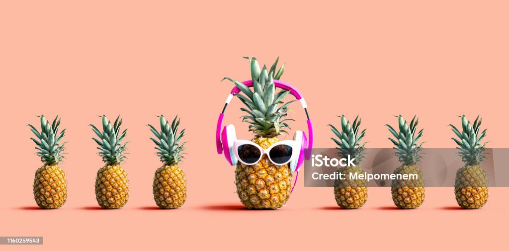 One out unique pineapple wearing headphones One out unique pineapple wearing headphones on a solid color background Standing Out From The Crowd Stock Photo