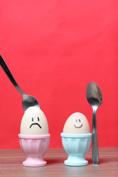 istock A boiled egg with a chopped shell stands in a poached. On the egg painted smiley. A spoon is stuck in it for food. Against the background of coral color. 1160262187